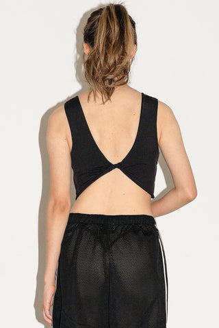 Woman in front of white background wearing a black tank top with twist detail and black mesh shorts. 