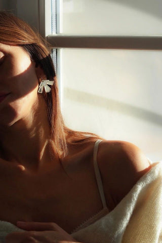 Woman in front of window wearing cream sweater and  silver mirror Lotus earrings by Mim Té. 