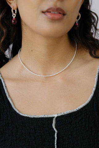 Close-up of woman wearing black top, silver & garnet earrings and silver and freshwater pearl necklace. 