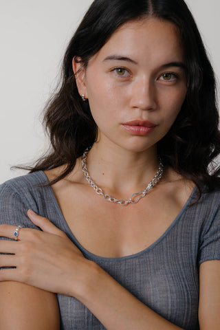 Close-up of woman wearing grey t-shirt and silver chain link necklace. 