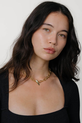 Close-up of woman wearing grey t-shirt and gold chain link necklace. 