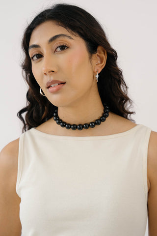 Close-up of woman wearing white tank top, silver earrings and large black onyx beaded collar necklace. 
