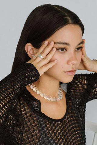 Close-up of woman wearing black mesh top, silver rings and large quartz beaded collar necklace. 