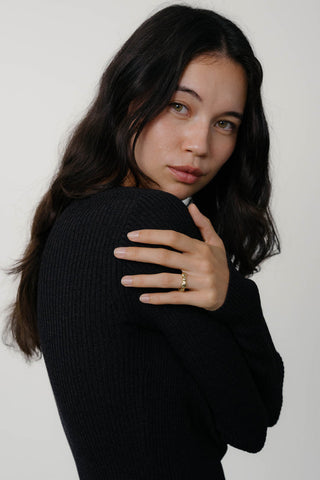 Side profile of woman wearing black sweater and gold plated ring. 