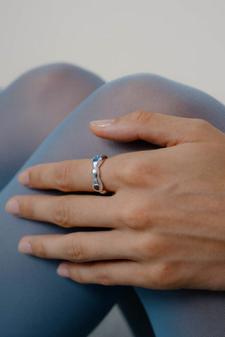 Close-up of woman's legs and hand, wearing wavy sterling silver ring with yellow, brown and blue gemstone. 