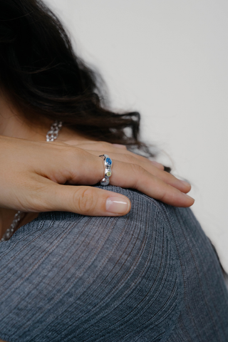 Close-up of woman's shoulder and hand, wearing wavy sterling silver ring with yellow, brown and blue gemstone. 
