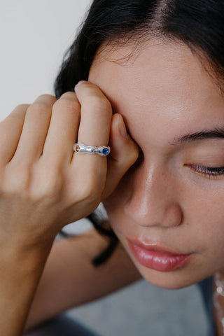 Close-up of woman's face & hand, wearing wavy sterling silver ring with yellow, brown and blue gemstone. 