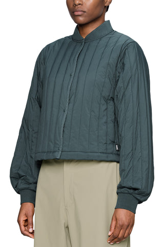A model wearing a dark teal quilted jacket with a stand-up collar and beige trousers, shown against a plain white background.