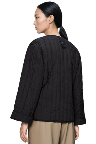 A woman shown from the back wearing a black quilted jacket, paired with beige trousers, against a plain white background.