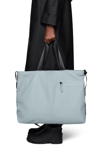 Person wearing black coat holding light blue messenger tote bag with carry handles. 