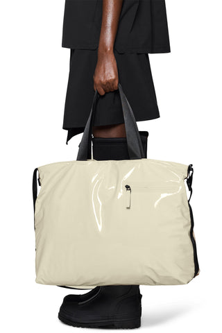 Person holding a shiny cream messenger tote bag with carry handles. 