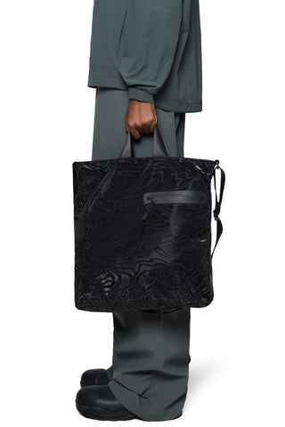 Person holding black tote bag with zippered front pocket. 