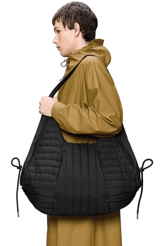 Person wearing camel rain jacket holding quilted black shoulder bag. 