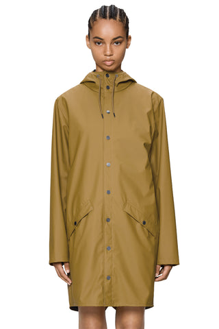 Woman in front of white background wearing camel coloured above knee raincoat. 