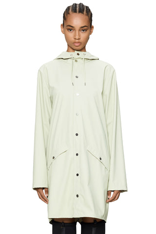 Woman in front of white background wearing cream coloured above knee raincoat. 