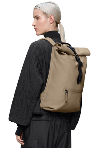 Woman with black jacket wearing dark beige roll top waterproof backpack. 
