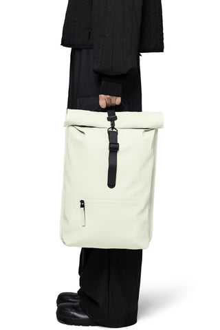 Side view of person holding waterproof cream coloured roll-top backpack. 
