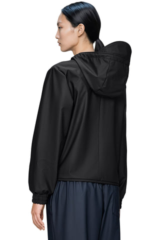 Back view of woman wearing a black hooded windbreaker jacket and dark navy pants against a plain white background.