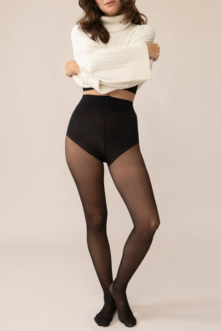 Woman in front of beige background wearing white sweater and black tights.