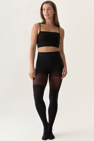 Woman in front of white background wearing black bra and black over-the-knee tights. 