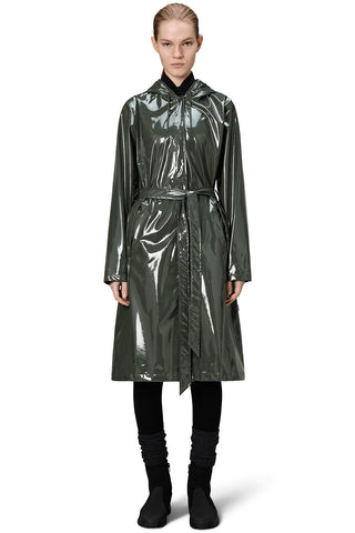 Woman, standing in front of white background, wearing shiny green (swamp) Aline belted Longer Jacket by RAINS. 