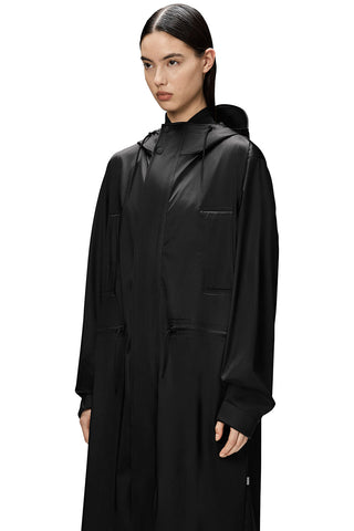 Close-up view of woman wearing black unisex waterproof and windproof full length Bold Longest Jacket by RAINS. 
