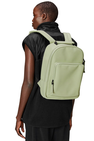 Woman wearing green (earth) waterproof minimal Book Daypack W3 by Rains. 