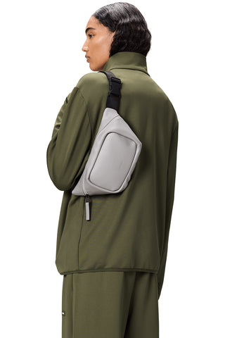 Woman in front of white background, back to camera, wearing green jacket and Nimbus grey Bum Bag Mini by RAINS. 