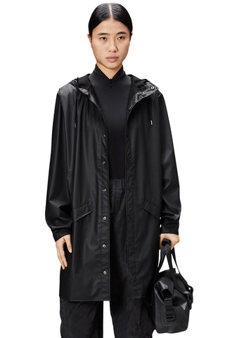 Woman wearing black waterproof Long Jacket by Rains. 