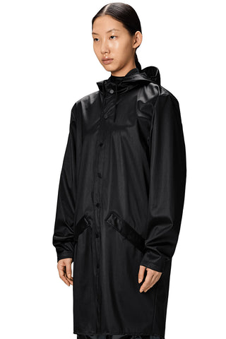 Close-up of woman wearing black unisex waterproof RAINS long jacket, against white background. 