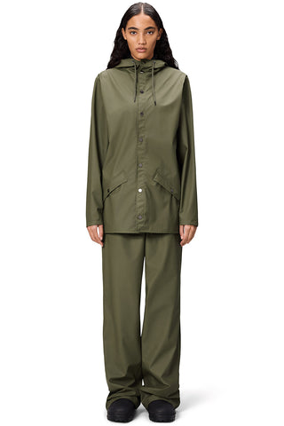 Woman standing in front of white background wearing Marsh (green) unisex waterproof RAINS jacket with matching pants. 