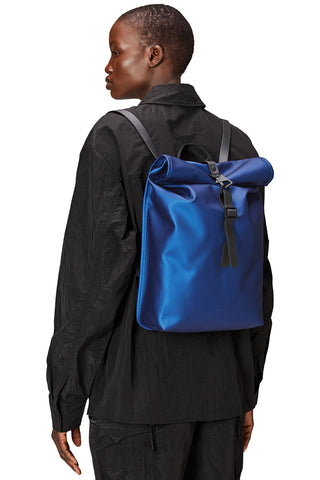 Woman wearing vibrant blue Roll Top Mini W3 backpack by RAINS. 