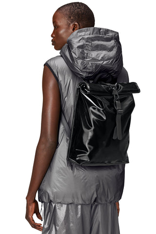 Woman wearing shiny black Roll Top Mini W3 backpack by RAINS. 