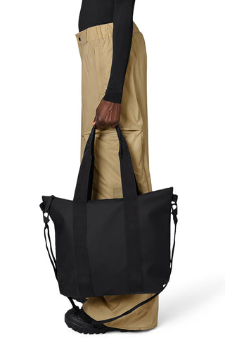 Woman carrying black waterproof Rains Tote Bag Mini. 