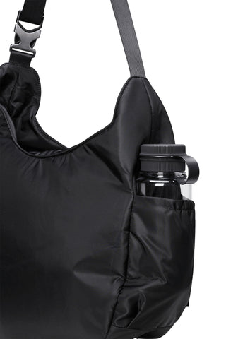 Close-up of a black nylon shoulder bag with a side pocket holding a black water bottle, against a light gray background.
