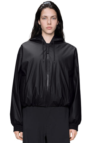 A model wearing a black hooded zip-up bomber style jacket and matching black pants, photographed against a plain white studio background.