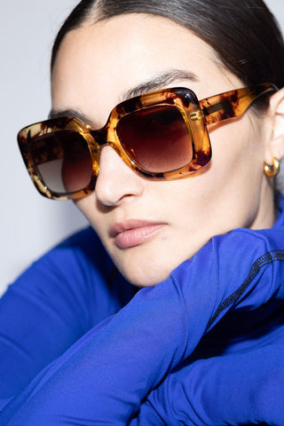 Woman wearing transparent tortoise shell oversized square shaped sunglasses. 