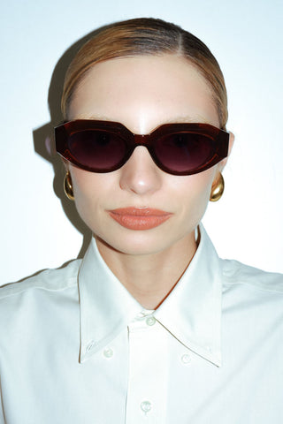 Woman wearing crisp white collared shirt and dark brown acetate sunglasses. 