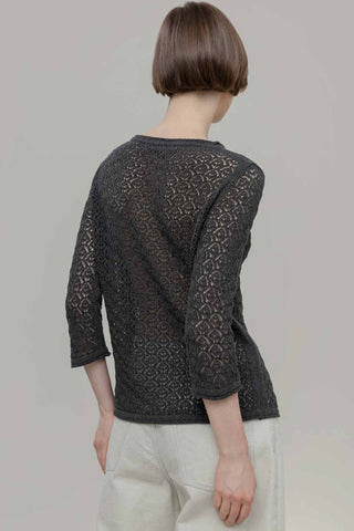 Back view of woman in front of plain background wearing 3/4 sleeve lace knit navy sweater with white pants.  