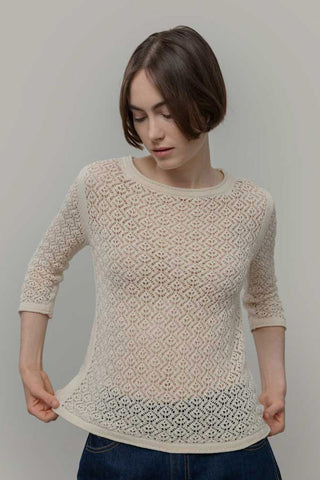 Woman in front of plain background wearing 3/4 sleeve lace knit cream sweater. 