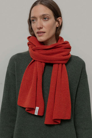 Woman in front of grey background wearing green knit sweater and orange knit Federico Scarf by Rifo. 