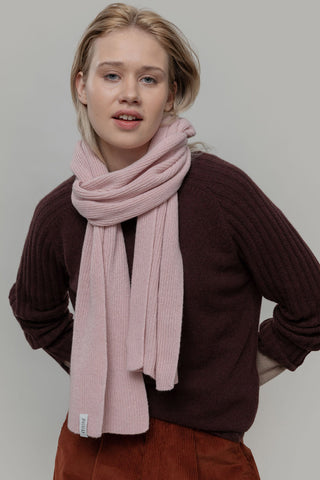 Woman in front of grey background wearing brown knit sweater and pink blush knit Federico Scarf by Rifo. 