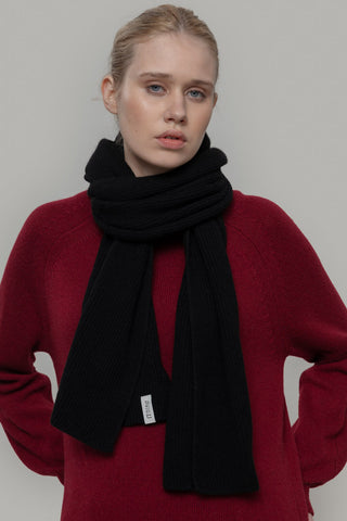 Woman in front of grey background wearing red knit sweater and black knit Federico Scarf by Rifo. 