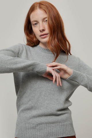 A woman with red hair wearing a light gray knit crewneck sweater, posing against a neutral light gray background.