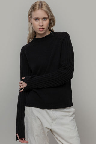 Woman in front of grey background wearing black knit Loretta sweater by Rifo. 