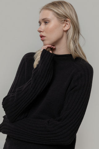 Woman in front of grey background wearing black knit Loretta sweater by Rifo. 