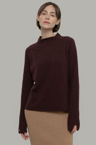 Woman in front of grey background wearing brown knit Loretta sweater by Rifo. 