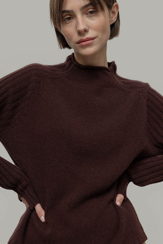 Woman in front of grey background wearing brown knit Loretta sweater by Rifo. 