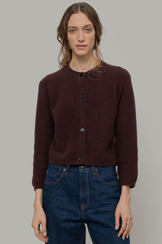 A woman wearing a brown knit cardigan with button-front closure, paired with blue jeans, against a solid gray studio background.