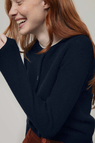 A close-up of a smiling woman with red hair wearing a dark navy knit cardigan.
